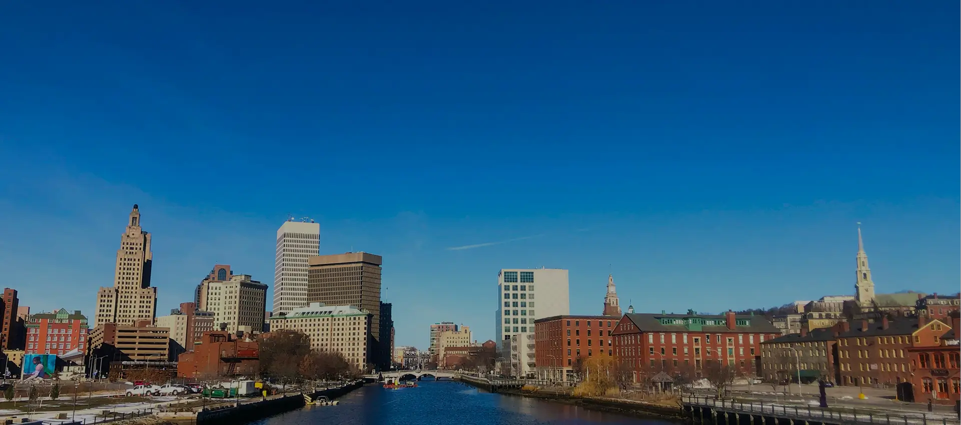 City skyline with buildings along a river under a clear blue sky.